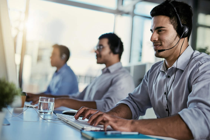 Three customer care executives with headphones, sitting in front of their systems, handling calls.